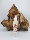 Eine Flasche „Rose Bulgarian Hydrosol“ Blütenwasser vor einem großen, strukturierten Stück Naturtreibholz auf weißem Hintergrund.