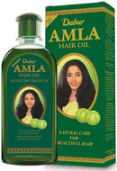 Eine Produktaufnahme, die eine grüne Flasche und die passende hohe, rechteckige Verpackung für Dabur Amla Hair Oil zeigt. Sowohl das Flaschenetikett als auch die Schachtel zeigen das Porträt einer Frau mit langen, dunklen Haaren und zwei Amla-Früchte (Indische Stachelbeere), beworben als „Natural Care for Beautiful Hair“.