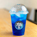Ein Plastikbecher zum Mitnehmen, gefüllt mit einem leuchtend blauen Eisgetränk auf einer Holzoberfläche.
