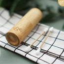 Zwei wiederverwendbare Wattestäbchen mit verschiedenen Silikonspitzen (strukturiert und glatt) liegen auf einem karierten Tuch neben einer Bambus-Transportbox mit Deckel.