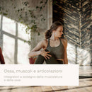 Eine Frau in einem Sport-BH führt in einem Studio mit unverputzten Ziegeln und Holzverkleidungen eine sitzende Yoga-Drehung aus. Das Bild enthält den italienischen Text: „Ossa, muscoli e articolazioni – Integratori a sostegno della muscolatura e delle osse“.