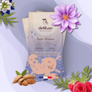 Eine "delikao Super Woman" Schokoladenverpackung lehnt auf einer weiteren Packung, umgeben von Mandeln, frischen Himbeeren und violetten Blumen auf einem weichen, violetten Hintergrund.