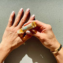 Draufsicht auf Hände, die PAAVANI AYURVEDA Tension Relief Oil mit einer Roll-on-Flasche auf den Handrücken auftragen.