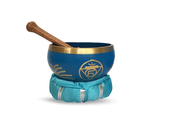 Eine blaue, goldverzierte Klangschale mit dem Vishuddha-Chakra-Symbol und Klöppel liegt auf einem türkisfarbenen Kissen.