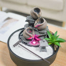 Ein Desktop-Zen-Garten mit einem dreistufigen Wasserbrunnen mit rosa LED-Lichtern und weißem Sand.