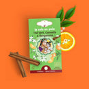 Die grüne und rote Schachtel Ayurvedischer Tee (Grüner Tee, Zimt, Bergamotte) liegt auf einer orangefarbenen Fläche, umgeben von Zimtstangen, Orangenscheiben und Blättern. Die Schachtel ist mit „Je suis en paix“ und 4 Chakra beschriftet.