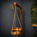 Ein hängendes Shirodhara-Gefäß aus Kupfer mit drei goldenen Ketten und einem Durchflussregelventil aus Messing am Boden.