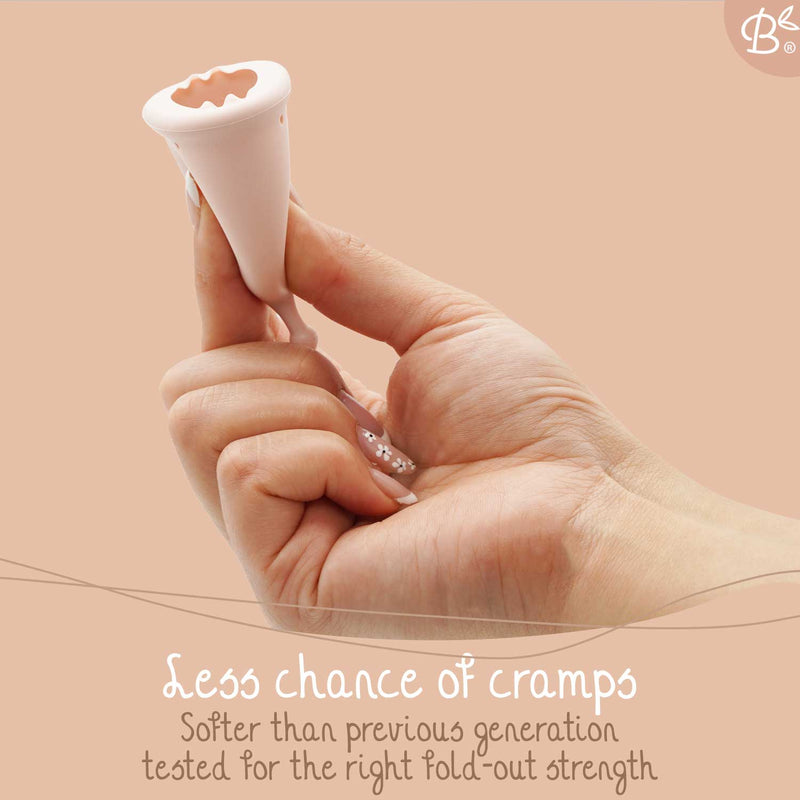 Eine Hand hält eine rosa Menstruationstasse und zeigt ihr flexibles Design. Der Text besagt "Geringere Krampfgefahr" und "Weicher als die vorherige Generation, getestet auf die richtige Entfaltungsstärke".