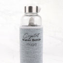 Eine durchsichtige Glaswasserflasche in einer grauen Stoffhülle mit Griff, die auf einer marmorierten Oberfläche steht. Auf der Hülle sind "Crystal Water Bottle" und "myga" in Schwarz aufgedruckt.