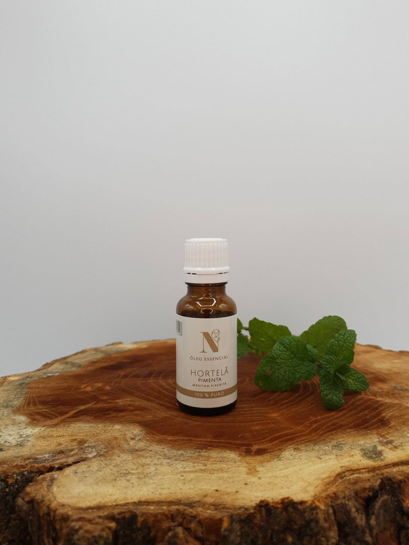 Kleine Flasche Pfefferminzöl (Hortelã Pimenta) auf einer Holzscheibe mit frischen Minzblättern.