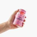 Eine Hand, die eine rosa Flasche Myga Kollagen-Gummis vor einem weißen Hintergrund hält.