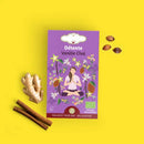 Eine Schachtel Détente Vanille Chai Tee mit Ingwer, Zimtstangen und Kardamomsamen auf gelbem Hintergrund.