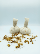 Zwei Kräuter-Massagebälle (Kräuterstempel) auf einem Haufen getrockneter Kamillenblüten und Salz.