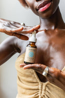 Eine dunkelhäutige Frau hält eine Flasche Paavani Ayurveda Pitta Serum für empfindliche Haut hoch.