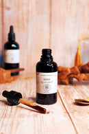 Eine dunkle Glasflasche mit Reishi-Flüssigextrakt und einer offenen Pipette auf einer hellen Holzoberfläche.