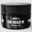 Ein schwarzes Glas mit "PURE SHILAJIT UK Himalayan resin", mit weißen Berg- und Textgrafiken.