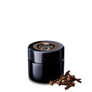 Eine schwarze Dose mit dem Etikett „Ancient Purity Cloves“ und ein paar Nelken daneben, auf einem weißen Hintergrund.