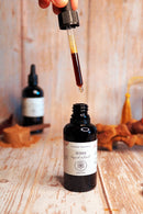 Eine Hand hält eine Pipette mit Flüssigextrakt über eine offene dunkle Glasflasche mit Reishi.