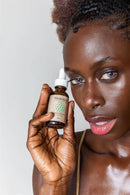 Eine Frau hält eine Flasche Paavani Ayurveda Vata Serum für trockene Haut neben ihr Gesicht.