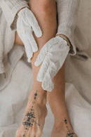 Eine Nahaufnahme der Beine einer Person, deren Hände weiße Trockenbürsthandschuhe tragen, und einer sichtbaren schwarzen Tätowierung auf einem Fuß.