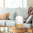 Aroma-Diffusor aus Holz und weißer Keramik, der Dampf abgibt, auf einem Holztisch vor einem Sofa.