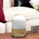 Aroma-Diffusor aus Holz und weißer Keramik mit aufsteigendem Dampf auf einem Holztisch im Wohnzimmer.