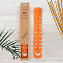 Oranger Räucherstäbchenhalter „Elm“ aus Holz mit silbernen Mondmotiven neben der Verpackung und Räucherstäbchen.