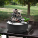 Desktop-Zen-Garten mit einem dreistufigen Wasserbrunnen, weißem Sand und einer kleinen Laternendekoration.