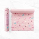 Eine rosa Myga Terrazzo Yogamatte, sowohl eingerollt in ihrer Papierhülle als auch teilweise ausgerollt mit einem bunten Steinchen-Muster.