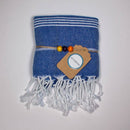 Ein gefaltetes blaues Handtuch mit weißen Quasten, gebunden mit einer Kordel und einem braunen ECOBAIN-Markenetikett mit gelben und orangen Perlen.