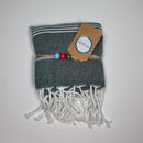 Ein gefaltetes dunkelgrau gemustertes Handtuch mit weißen Quasten, gebunden mit einer Schnur und einem „ECOBAIN“-Etikett.