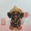 Eine dunkelbraune Statue des meditierenden Lord Ganesha, geschmückt mit einer goldenen Krone und Schmuck.