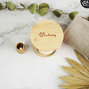 Ein Bambushalter mit weißen wiederverwendbaren Wattepads, ein kleiner Bambusbehälter mit Wattestäbchen und ein gefaltetes beiges Handtuch, alles auf einer Marmoroberfläche mit einer grünen Pflanze.