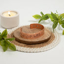 Magnetischer Kupfer-Armreif mit graviertem Muster auf einer Holzscheibe und Untersetzer mit Kerze