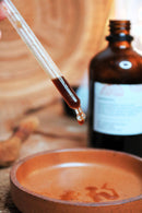 Eine mit dunklem Flüssigextrakt gefüllte Glaspipette über einer flachen Holzschale.