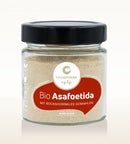 Ein klares Glas mit Cosmoveda Bio-Asafoetida (Hing), gemahlen mit Bockshornklee und schwarzem Deckel. Das Etikett trägt die Aufschrift "Bio Asafoetida mit Bockshornklee gemahlen" und „mixed spices."