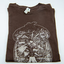 Ein gefaltetes, braunes T-Shirt mit einem weißen Aufdruck eines großen Pilzes, dessen Kappe eine detaillierte Landschaft mit einem zentralen Baum und einem Sonnenstrahl umschließt.