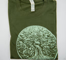 Ein gefaltetes, dunkelolivgrünes T-Shirt mit einem hell- und dunkelgrünen Motiv eines dickstämmigen Baumes, dessen Blätterdach einem Gehirn ähnelt.