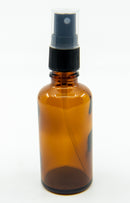 Eine klare, bernsteinfarbene Glas-Sprühflasche mit schwarzem Zerstäuberkopf und transparenter Kunststoffkappe, fotografiert vor weißem Hintergrund.