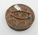 Ein Armband aus Sandelholz- und sieben Chakra-Perlen, das auf einem runden, dunkelbraunen hölzernen Druckstempel mit geschnitztem Mandala-Muster liegt.