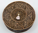 Ein kleiner, tropfenförmiger Rosenquarz-Anhänger, der auf einem runden, dunkelbraunen hölzernen Druckstempel mit detailliertem Mandala-Muster liegt.