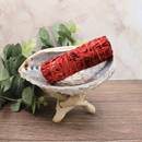 Dragons Blood Salbei Räucherbündel liegt in einer Muschelschale auf Holzoberfläche, dekorativ arrangiert für Räucherrituale und Raumreinigung.