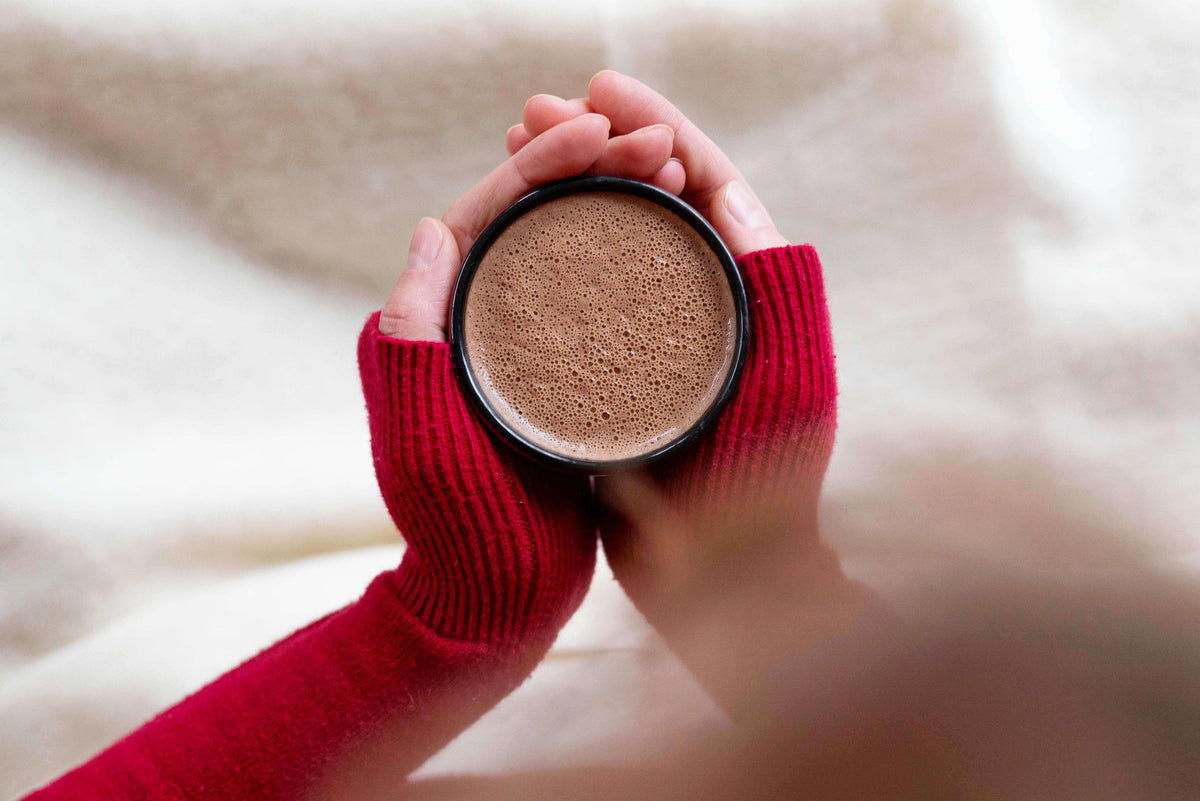 Hände in rotem Strickpullover halten Tasse mit schaumigem Bio-Schokoladengetränk für gesunden Lifestyle