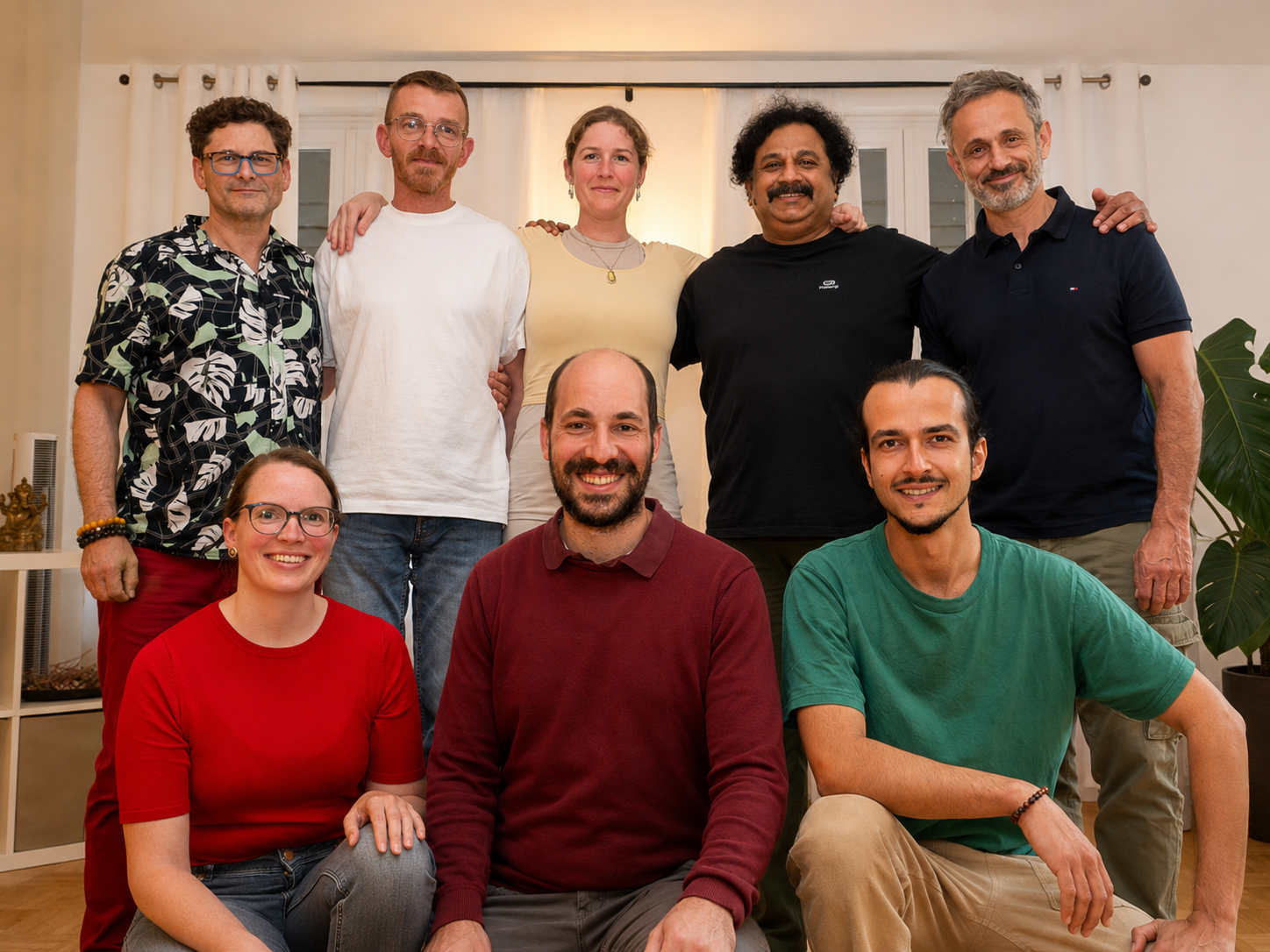 Gruppenfoto von acht Personen in einem hellen Raum. Fünf Personen stehen hinten und drei sitzen vorne. Die Gruppe lächelt freundlich in die Kamera und wirkt vertraut und gemeinschaftlich.