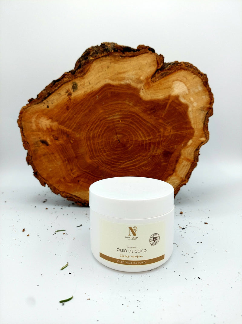 Weißer Tiegel mit N'Natureza „Óleo de Coco“ (Kokosöl), zentriert vor einem großen, grob geschnittenen, natürlichen Holzscheiben-Hintergrund.