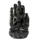 Eine schwarze, sitzende Buddha-Statue vor einer großen, aufrechten offenen Handfläche, ruhend auf einem dekorativen Lotussockel vor weißem Hintergrund.