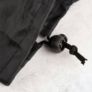 Eine Nahaufnahme des schwarzen Kordelzugs und der Kordelstopper einer schwarzen Yogamatten-Tasche, auf einer hellgrauen, marmorartigen Oberfläche.