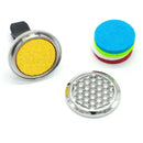 Einzelteile eines Auto-Diffusor-Sets: Ein offener Diffusor-Clip, der Deckel mit Blume des Lebens-Muster und ein Stapel farbiger Filz-Pads.