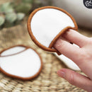 Eine Hand steckt einen Finger in die Tasche eines weißen wiederverwendbaren Wattepads mit braunem Rand und zeigt dessen Design.