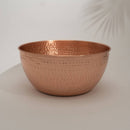 Große, runde gehämmerte Kupferschale auf einem schlichten Hintergrund mit einem Blattschatten.